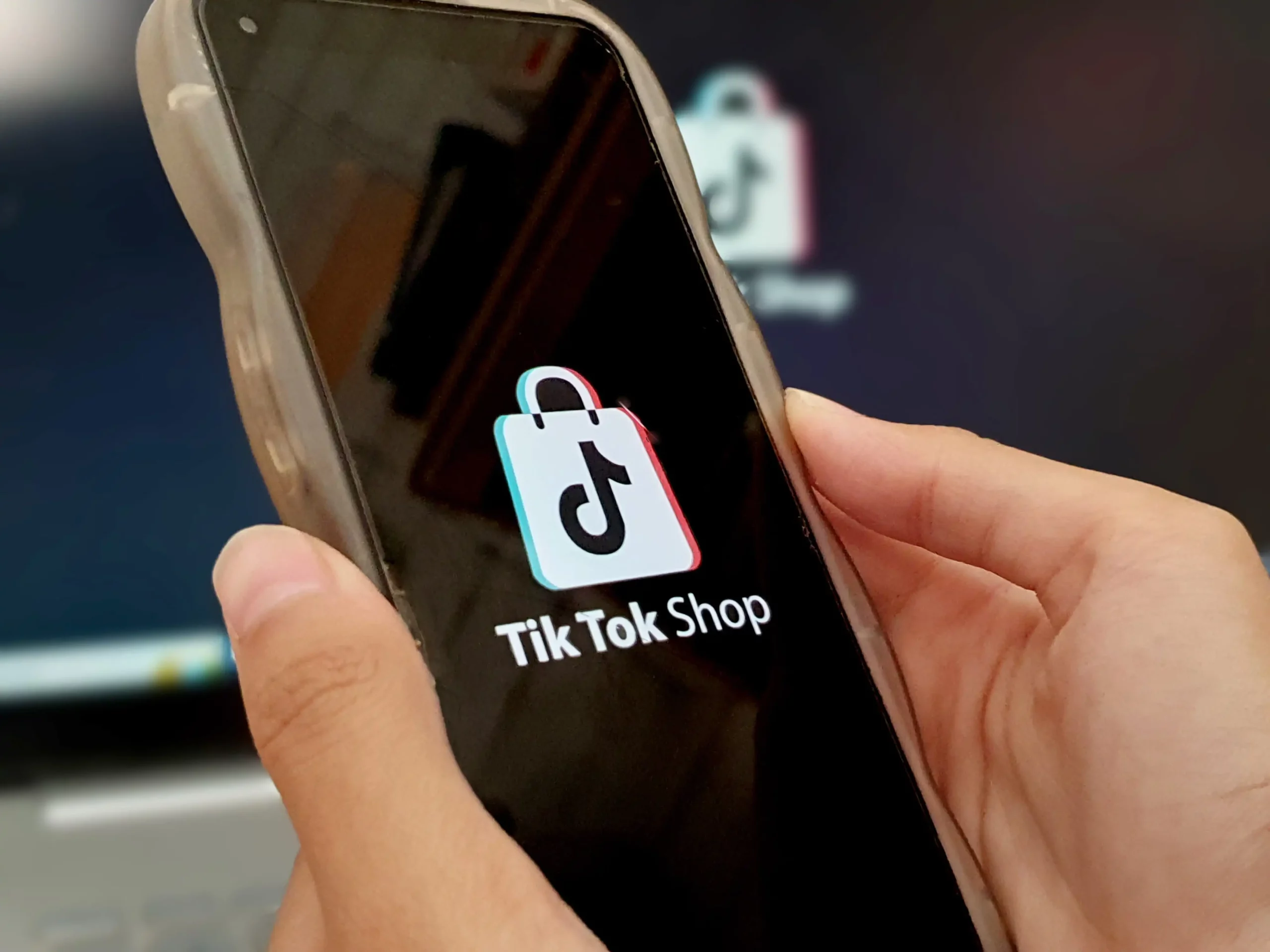 Zbliżenie na dłonie trzymające smartfon, na ekranie którego wyświetla się oficjalne logo aplikacji TikTok Shop.